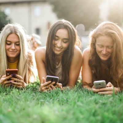 female friends browsing smartphone on lawn